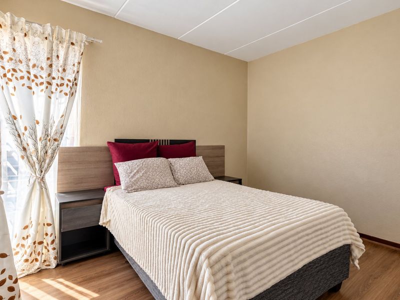 A well-maintained bedroom featuring warm-toned walls, laminate flooring, and a built-in headboard with integrated side tables.