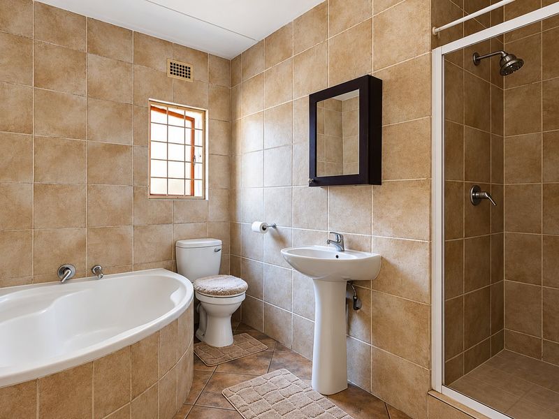 A functional bathroom featuring a pedestal basin, built-in bathtub, separate shower enclosure, and neutral wall-to-floor tiling.