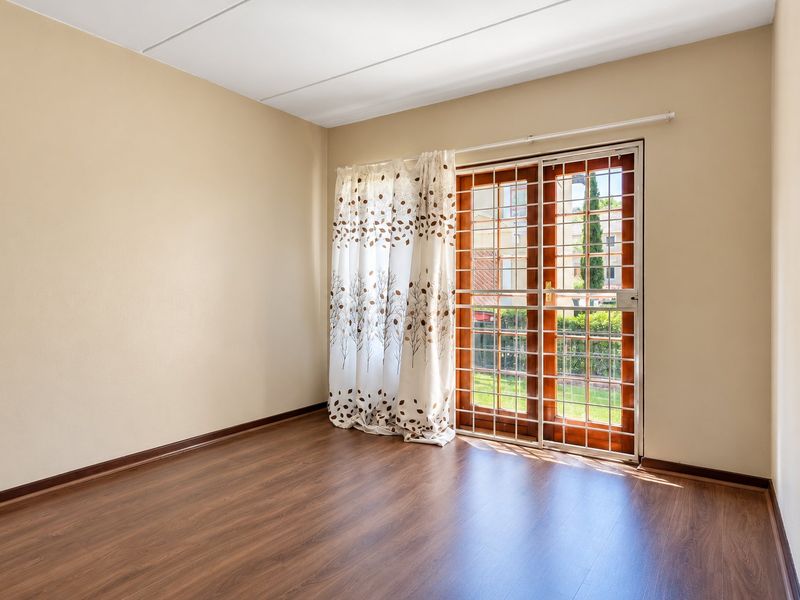 An empty bedroom featuring laminate flooring and a sliding glass door with a security gate, providing direct access to the outdoor area.