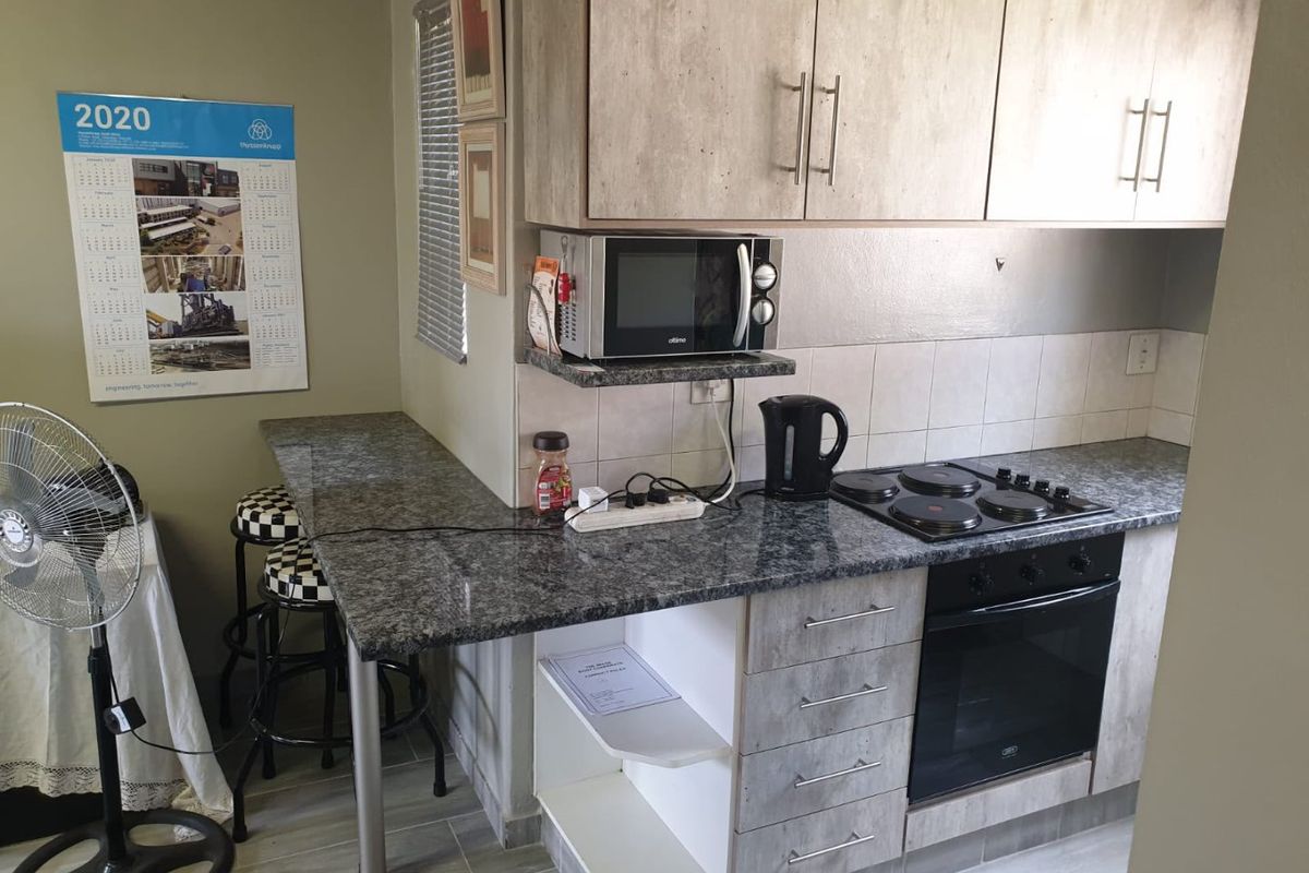 Compact kitchen featuring modern wood-look cabinetry, granite countertops, a built-in electric oven and hob, and an integrated breakfast bar.