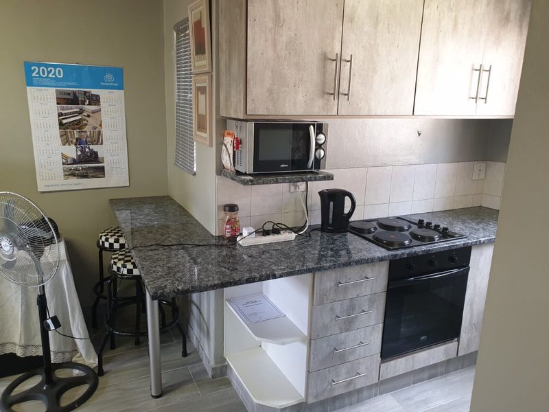 Compact kitchen featuring modern wood-look cabinetry, granite countertops, a built-in electric oven and hob, and an integrated breakfast bar.