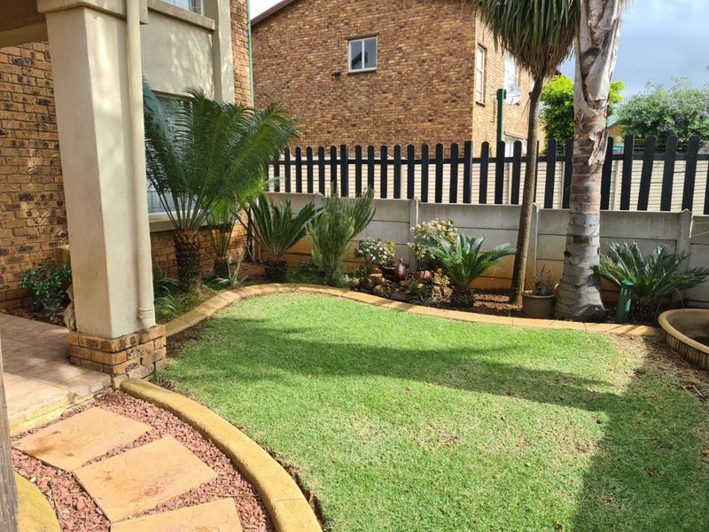 A well-maintained rear garden featuring a manicured lawn, paved walkway, and a covered patio area, enclosed by a secure precast concrete boundary wall.