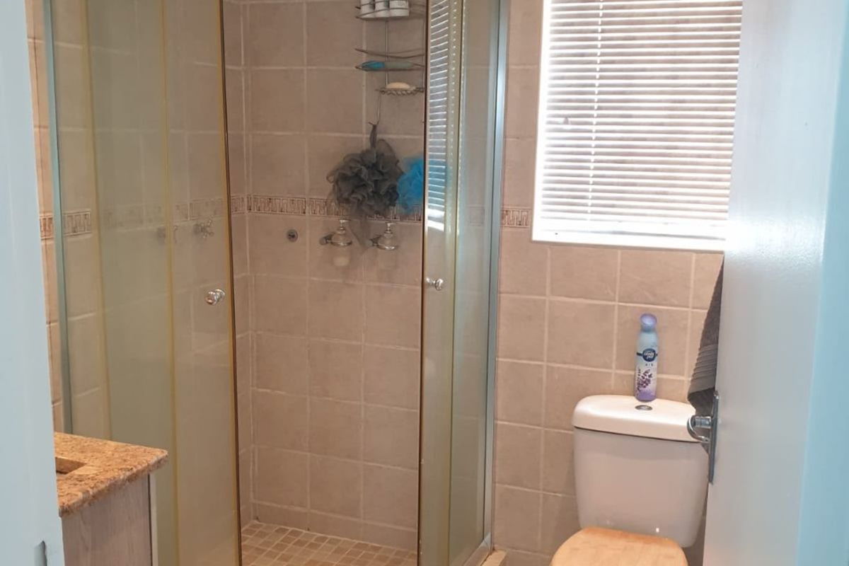 A functional bathroom featuring a curved glass shower enclosure, tiled finishes, a vanity with granite countertop, and a standard toilet.