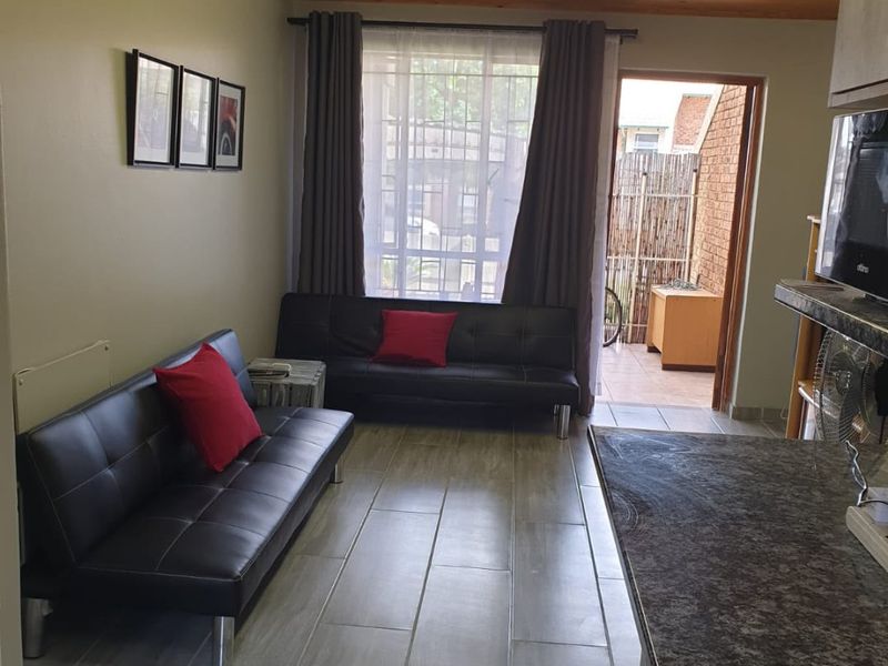 Open plan living area featuring tiled floors, timber ceiling, and a functional kitchen with granite countertops, leading out to a small patio area.