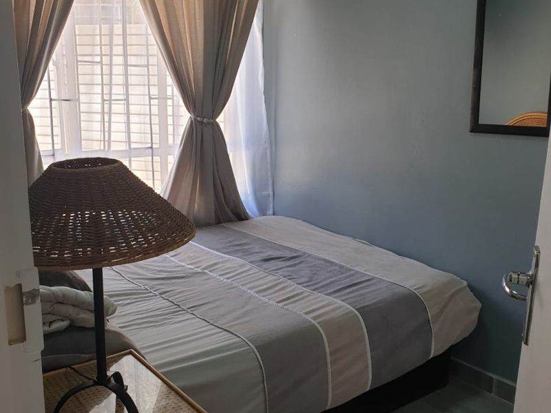 A compact bedroom featuring tiled flooring and a window fitted with security bars, offering a functional and private sleeping space.
