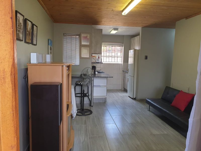 Open-plan living and kitchen area featuring tiled flooring, timber ceiling, and functional kitchen cabinetry with a breakfast counter.