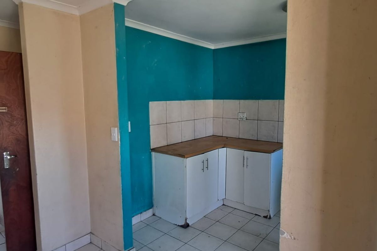 A compact kitchen area featuring built-in cabinetry, tiled splashbacks, and tiled flooring, currently in need of cosmetic updates and maintenance.