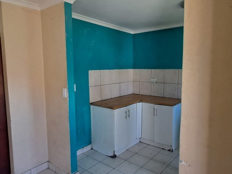 A compact kitchen area featuring built-in cabinetry, tiled splashbacks, and tiled flooring, currently in need of cosmetic updates and maintenance.
