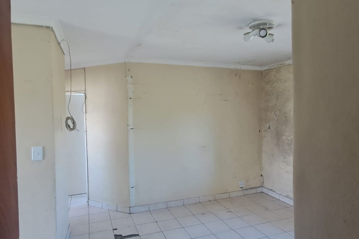 An empty living area featuring tiled flooring and ceiling lighting, currently requiring significant wall and floor repairs to restore the space.