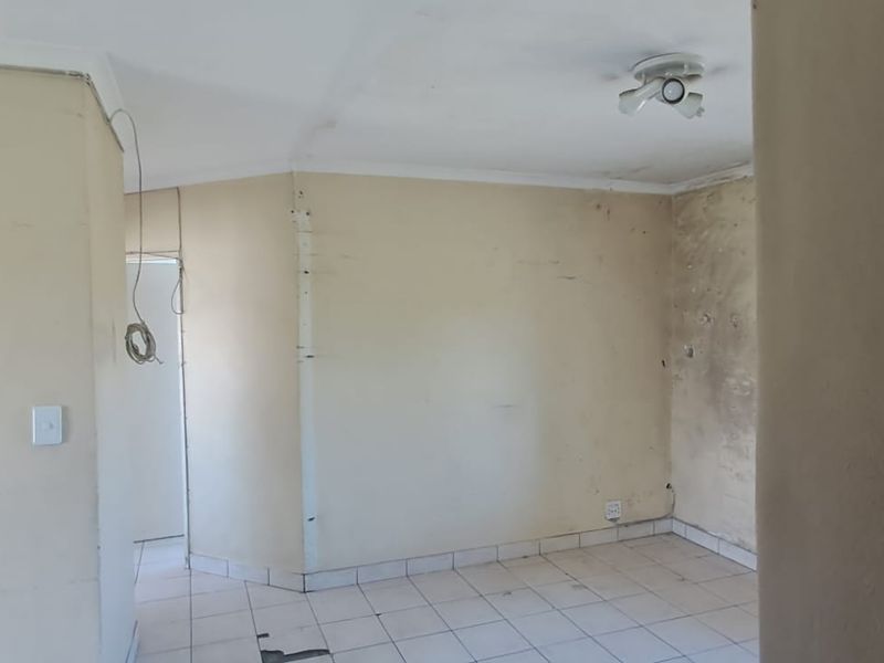 An empty living area featuring tiled flooring and ceiling lighting, currently requiring significant wall and floor repairs to restore the space.