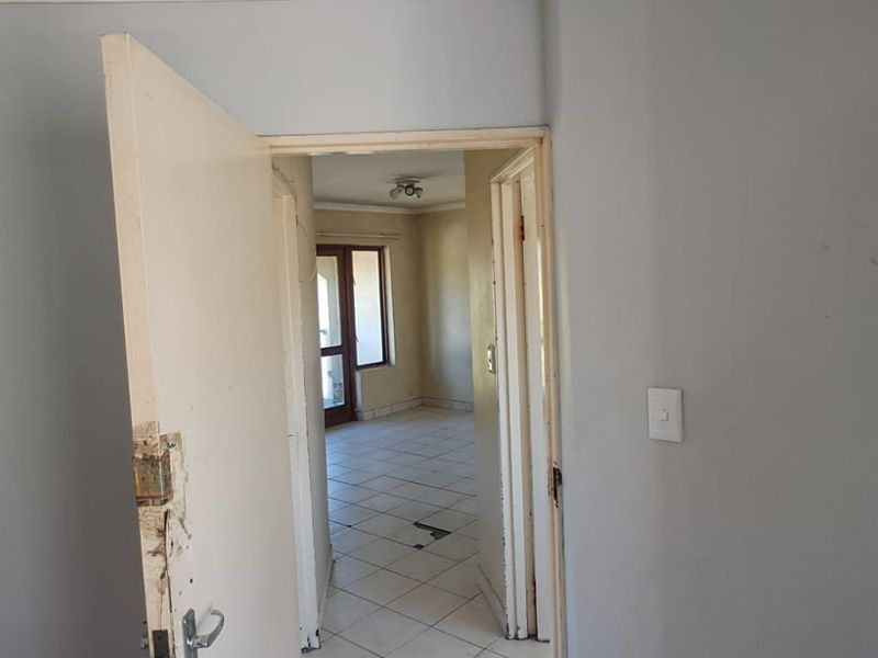 A view through a hallway into an adjacent room, featuring tiled flooring and visible wear on the door frame and finishes.