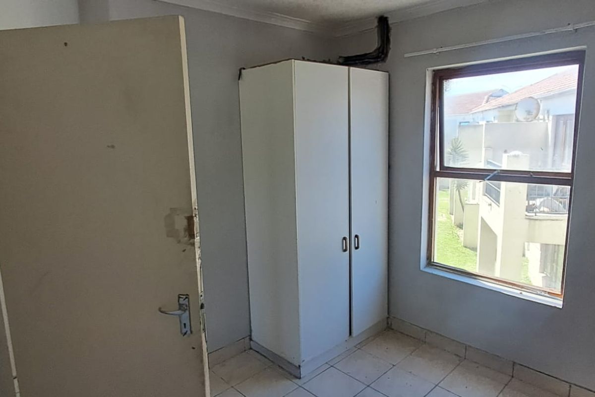A compact bedroom featuring tiled flooring, a built-in cupboard, and a window with views of the surrounding complex.
