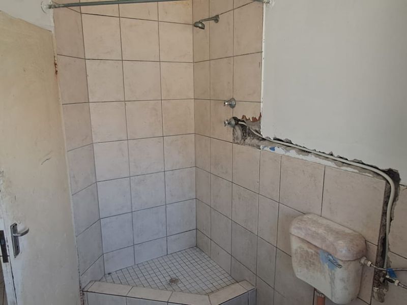 A bathroom in need of renovation, featuring a tiled shower cubicle and exposed plumbing, requiring repairs to wall finishes and fixtures.