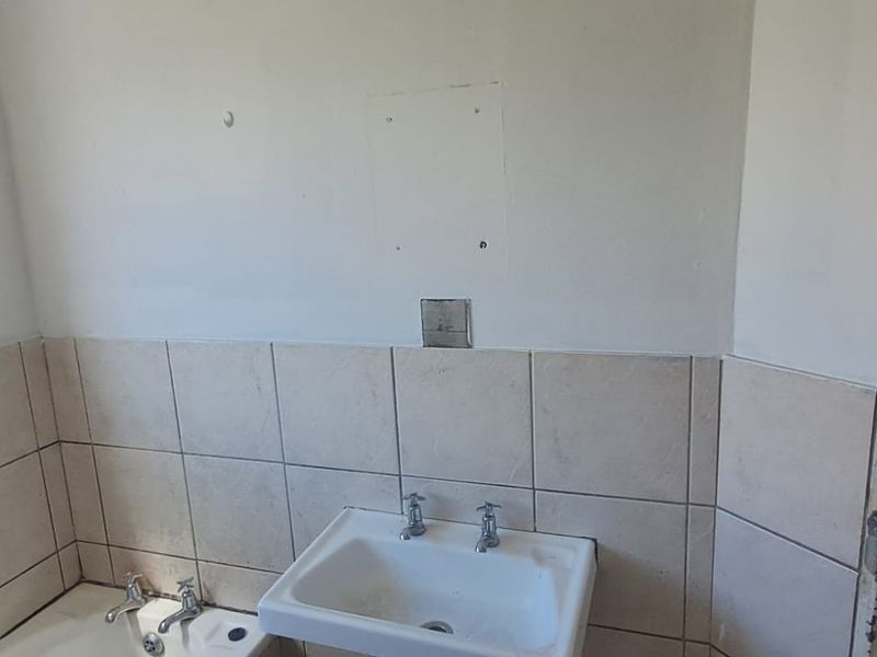 A functional bathroom featuring a pedestal washbasin, bathtub, and partial wall tiling, requiring cosmetic updates to improve its overall condition and appeal.