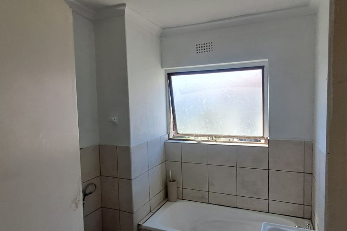 A compact bathroom featuring a built-in bathtub, tiled walls, and a top-hung window, currently in need of cosmetic updates and maintenance.