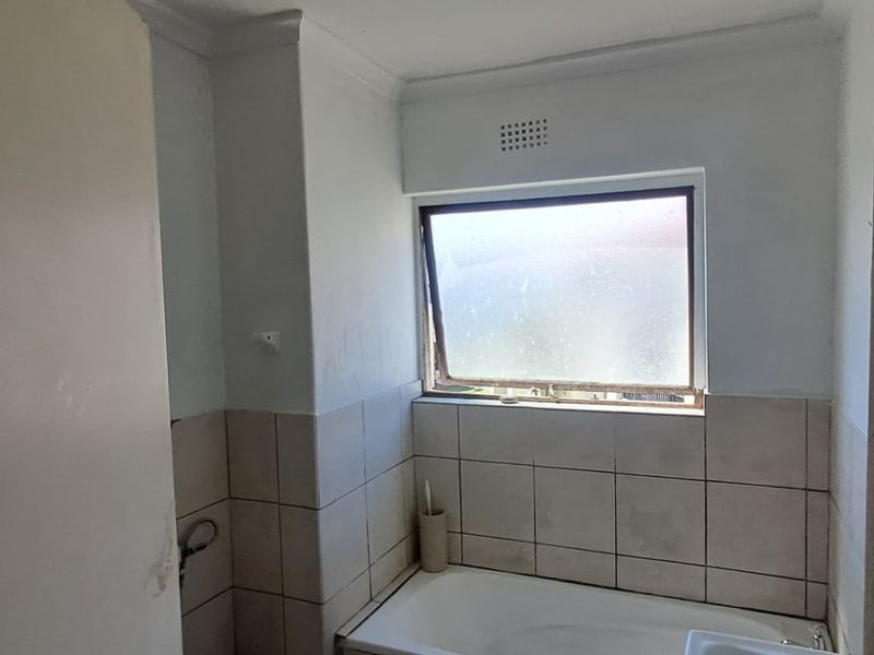 A compact bathroom featuring a built-in bathtub, tiled walls, and a top-hung window, currently in need of cosmetic updates and maintenance.