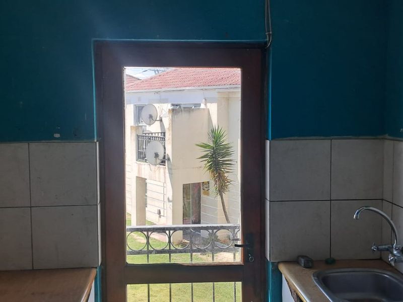 A functional scullery area featuring a stainless steel sink, tiled splashback, and an integrated electrical distribution board, with direct access to the exterior.