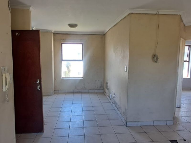 An empty living area featuring tiled flooring and coving, requiring cosmetic updates and repairs to walls and electrical fixtures.
