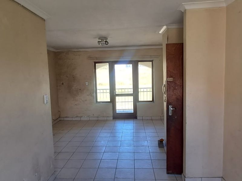 An empty living area featuring tiled flooring and a sliding glass door leading to an exterior space, requiring cosmetic updates to the wall finishes.