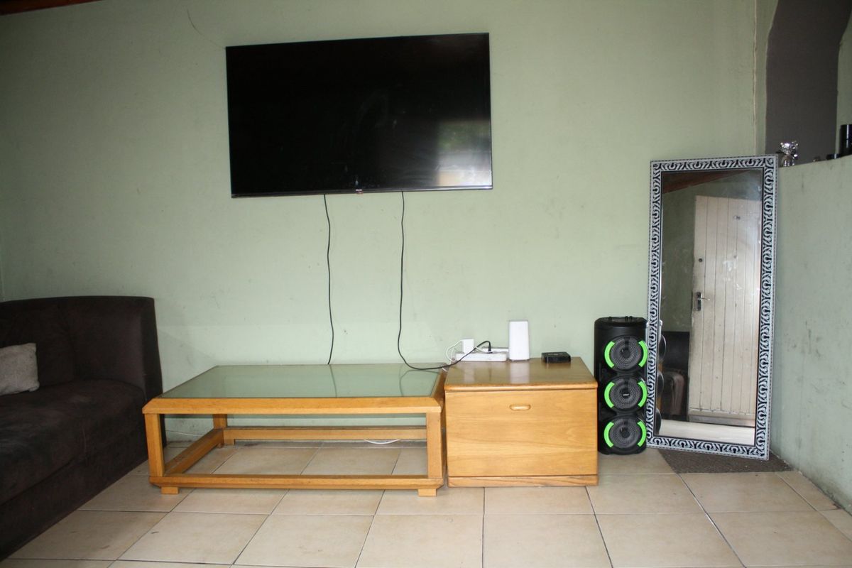 A living room area featuring tiled flooring and a wall-mounted television, requiring minor cosmetic updates to the wall finishes.