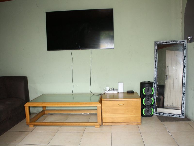 A living room area featuring tiled flooring and a wall-mounted television, requiring minor cosmetic updates to the wall finishes.