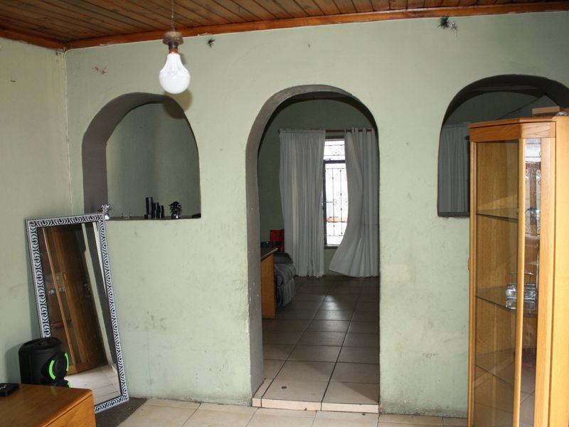 Living area featuring distinctive arched wall openings, ceramic floor tiles, and a timber tongue and groove ceiling, requiring cosmetic updates to improve presentation.