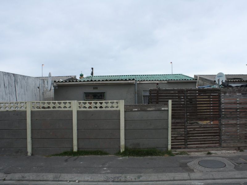 Front exterior view of a single-story residence featuring a precast concrete boundary wall, timber gate, and corrugated metal roofing.