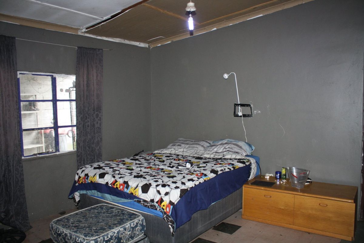 A bedroom featuring dark painted walls, steel window frames, and exposed ceiling panels requiring maintenance and cosmetic updates.