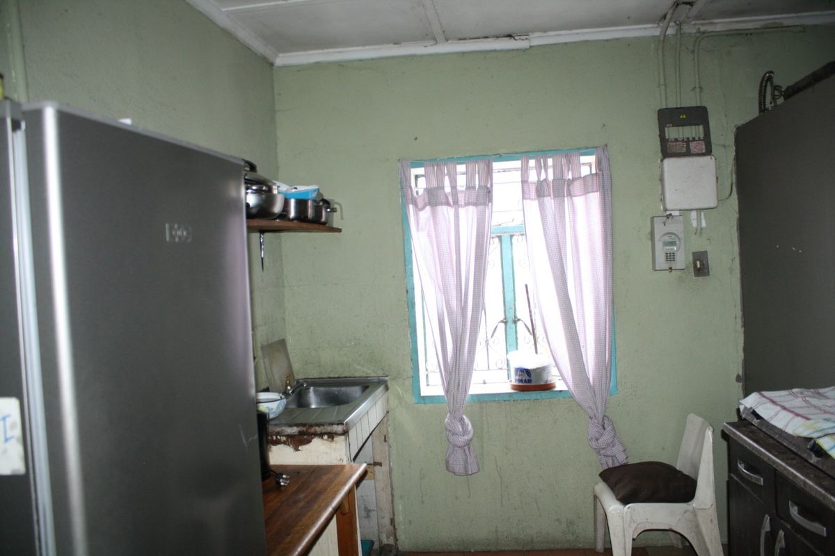 A dated kitchen area featuring a stainless steel sink, tiled splashback, and visible electrical infrastructure, requiring cosmetic updates and finish repairs.
