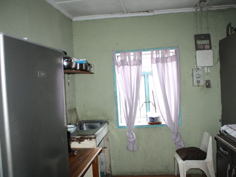 A dated kitchen area featuring a stainless steel sink, tiled splashback, and visible electrical infrastructure, requiring cosmetic updates and finish repairs.