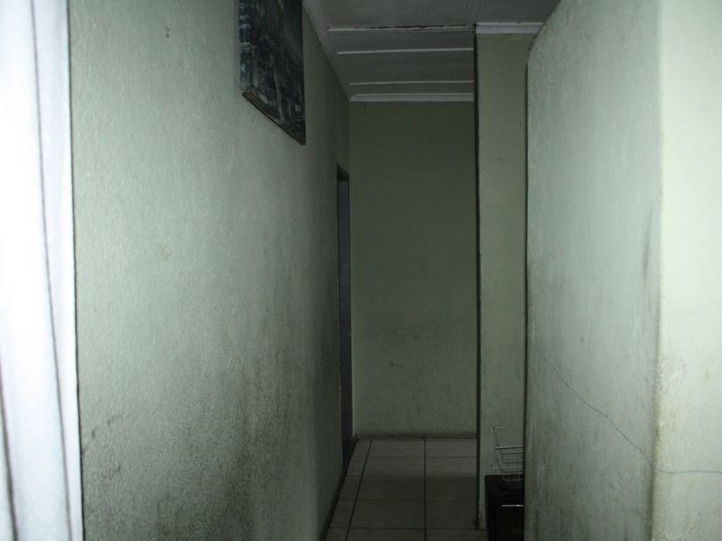 A narrow interior hallway featuring tiled flooring and plain walls showing signs of significant wear and surface staining.