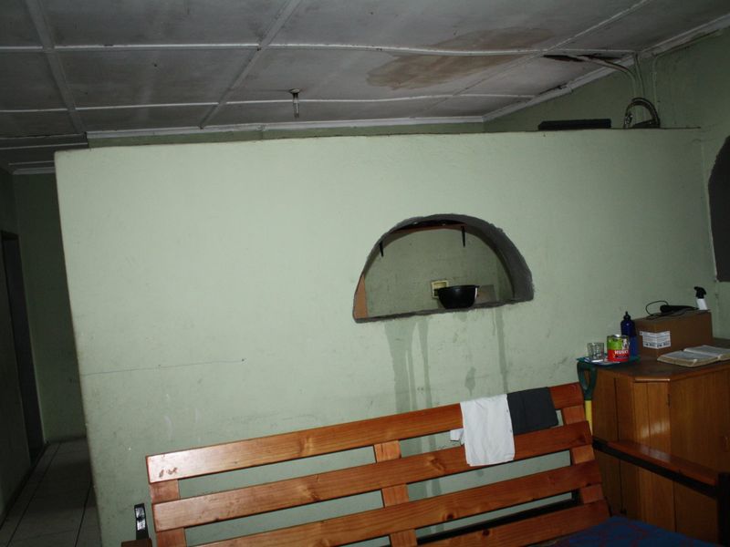 A living area featuring a distinctive arched wall cutout, tiled flooring, and a suspended ceiling, currently showing significant signs of water damage and wear.