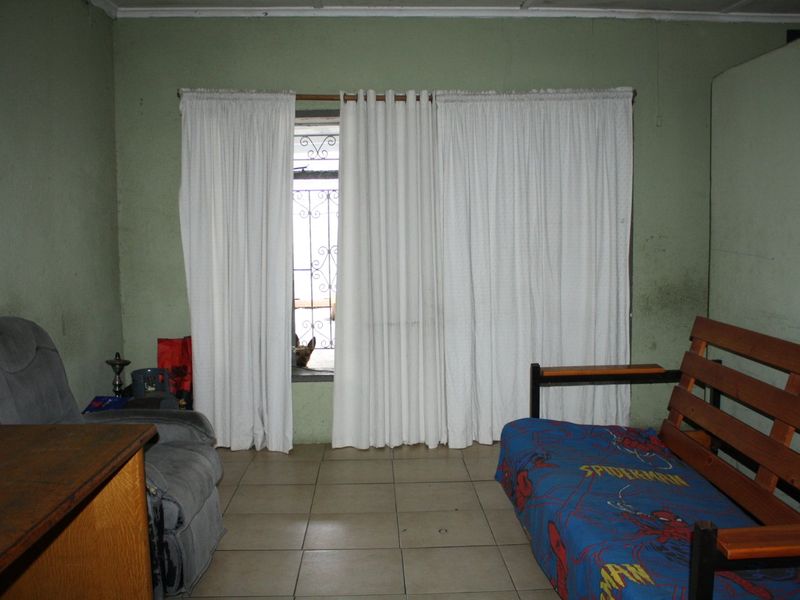 A living room space featuring tiled flooring and security gate access, currently requiring cosmetic updates and wall repairs to improve the overall condition.