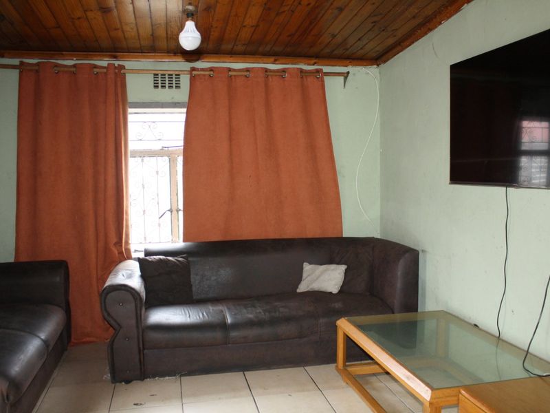 A living room featuring tiled flooring and a timber tongue and groove ceiling, with security bars installed on the window.