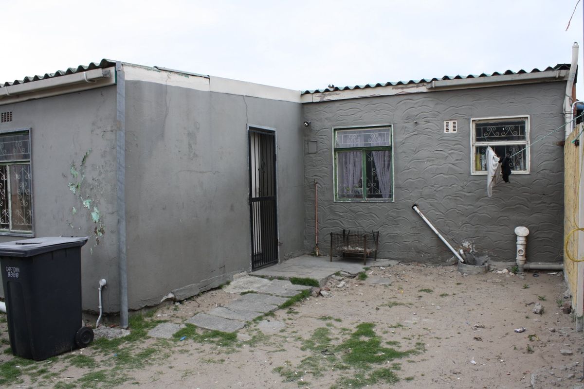 Rear exterior view of the property showing a plastered facade, security features, and basic outdoor area requiring maintenance.