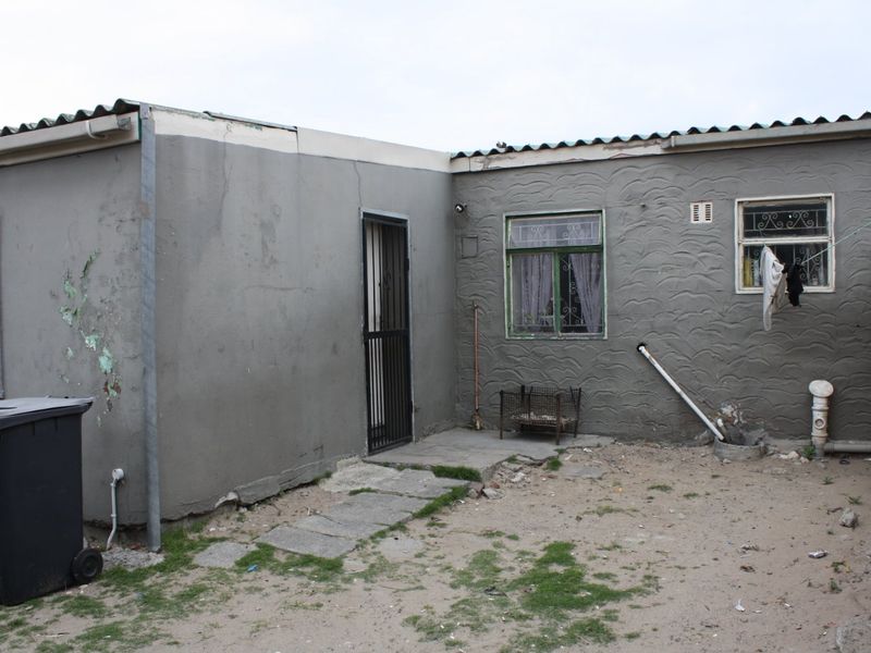 Rear exterior view of the property showing a plastered facade, security features, and basic outdoor area requiring maintenance.