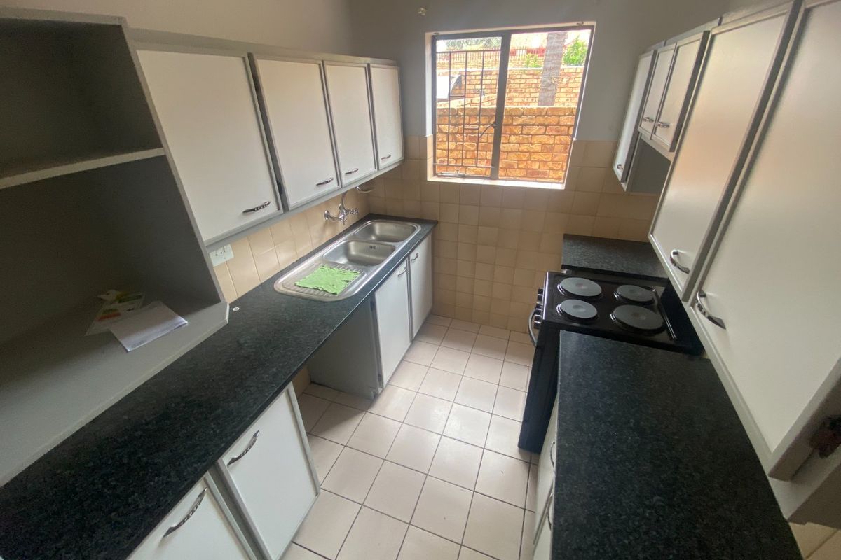 A functional kitchen featuring white built-in cabinetry, dark granite countertops, a double basin sink, and tiled flooring with a window overlooking the exterior.