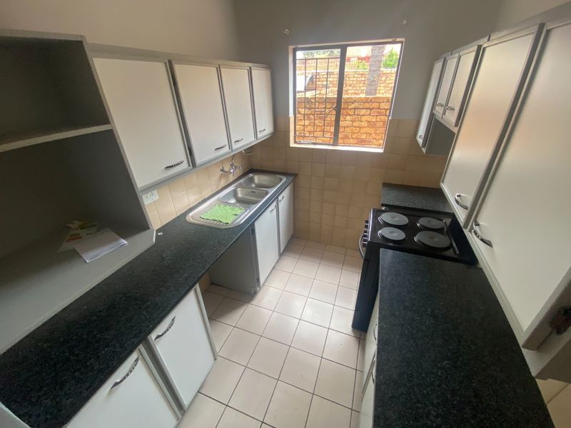 A functional kitchen featuring white built-in cabinetry, dark granite countertops, a double basin sink, and tiled flooring with a window overlooking the exterior.