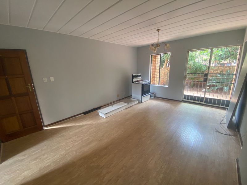 An open-plan living area featuring laminate flooring, a panelled ceiling, and a sliding door with security gate leading to the exterior.