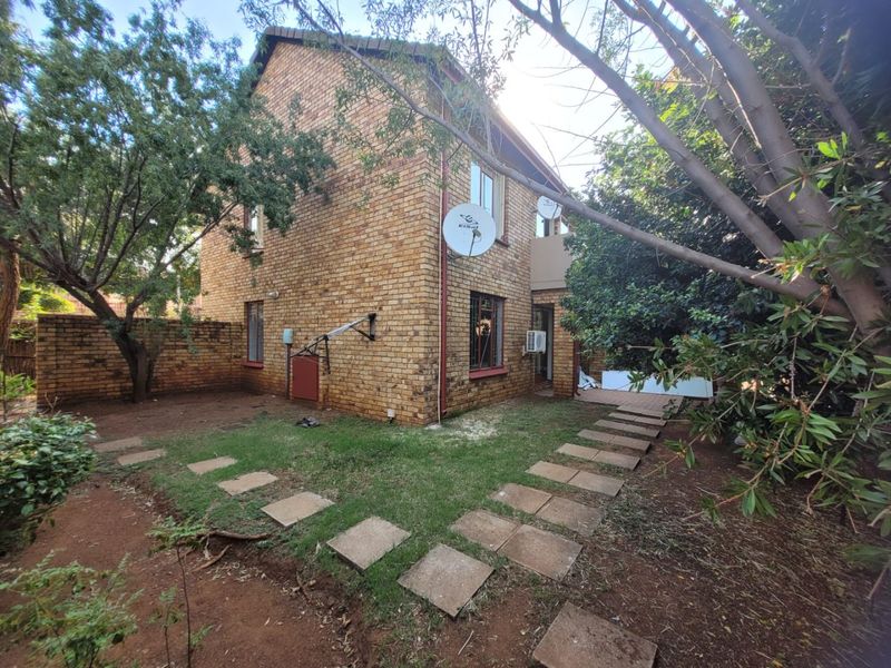 Rear view of a face brick apartment building featuring a private garden area with a paved walkway and established trees.
