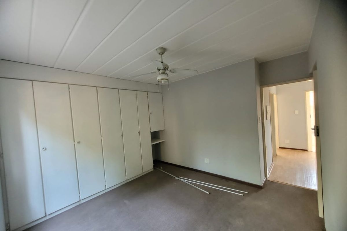 An empty bedroom featuring extensive built-in cupboards, a ceiling fan, and a panelled ceiling, offering a blank canvas for renovation.