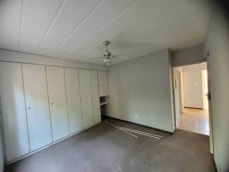 An empty bedroom featuring extensive built-in cupboards, a ceiling fan, and a panelled ceiling, offering a blank canvas for renovation.