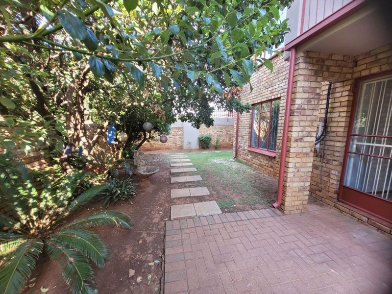 A rear exterior view of the apartment featuring a brick facade, paved patio area, and a garden path leading through the backyard.