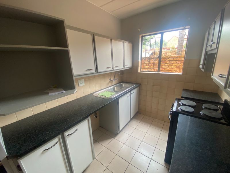 A functional kitchen featuring built-in cabinetry, double bowl sink, tiled backsplash, and tiled flooring with a window providing natural light.