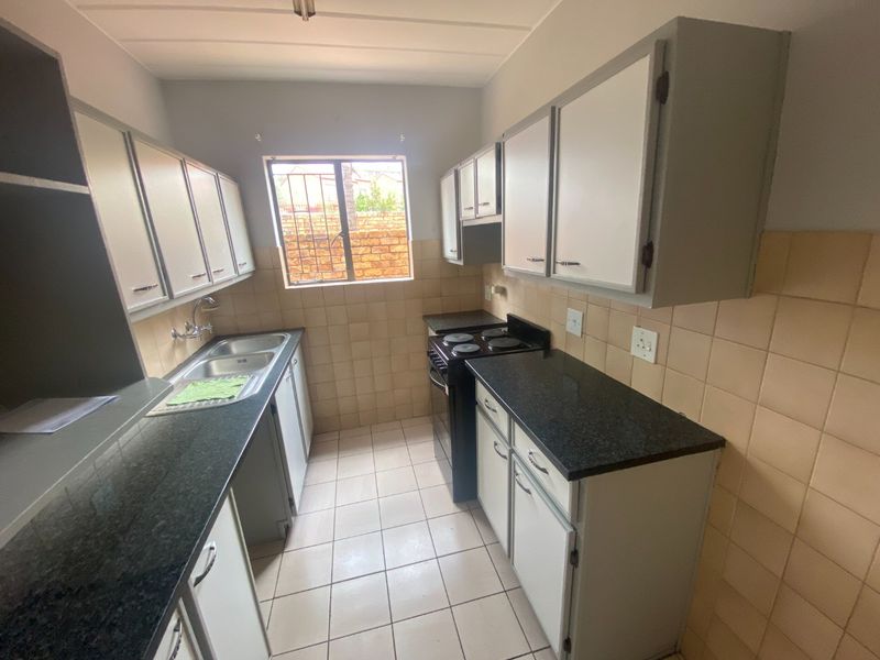 A functional galley-style kitchen featuring granite countertops, ample built-in cabinetry, a double basin sink, and tiled finishes throughout.
