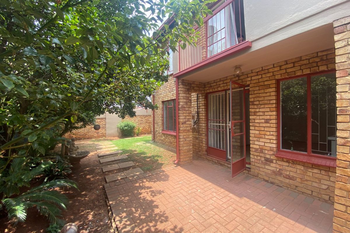 Rear view of the apartment featuring a face brick facade, a paved patio area, and an upper-level balcony overlooking a small garden.