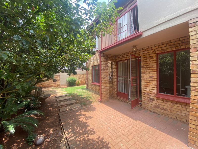 Rear view of the apartment featuring a face brick facade, a paved patio area, and an upper-level balcony overlooking a small garden.