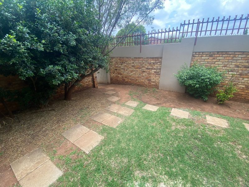 A private garden area featuring a brick boundary wall with security spikes, paved stepping stones, and established greenery.