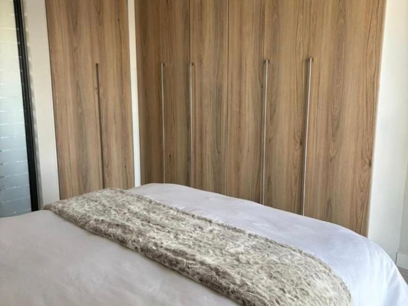 A well-maintained bedroom featuring floor-to-ceiling wood-finish built-in cupboards and a modern pendant light fixture.