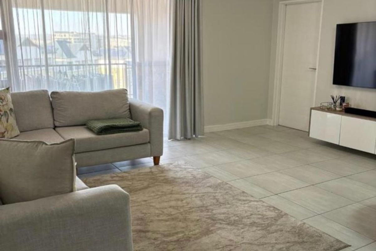 A bright and well-maintained living room featuring neutral tiled flooring, large sliding glass doors with curtains, and clean finishes throughout.